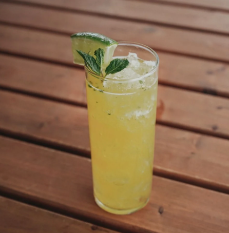 Yellow cocktail in tall glass with mint and lime garnish on a wooden table