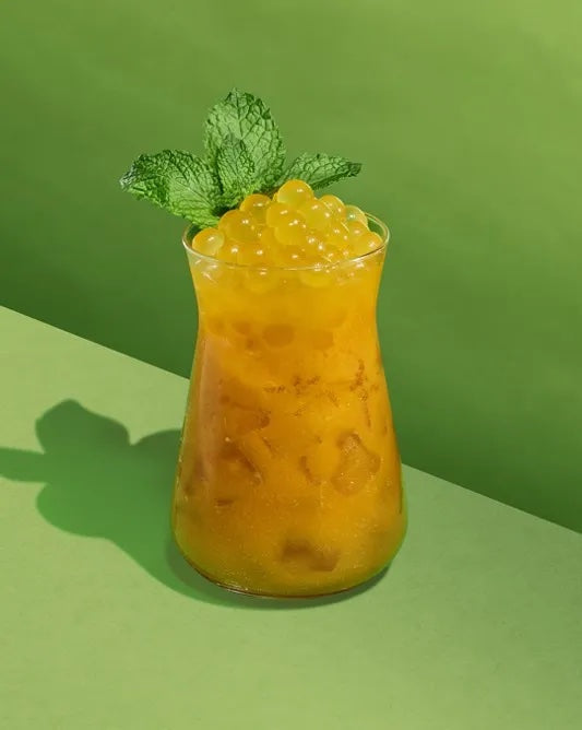 Yellow cocktail garnished with mint and boba against a lime green background