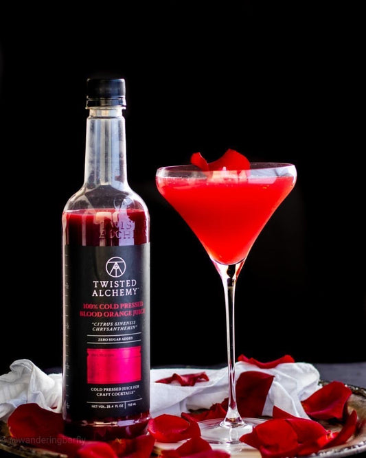 Blood orange cocktail in coupe glass with red rose petals and next to a blood orange juice bottle