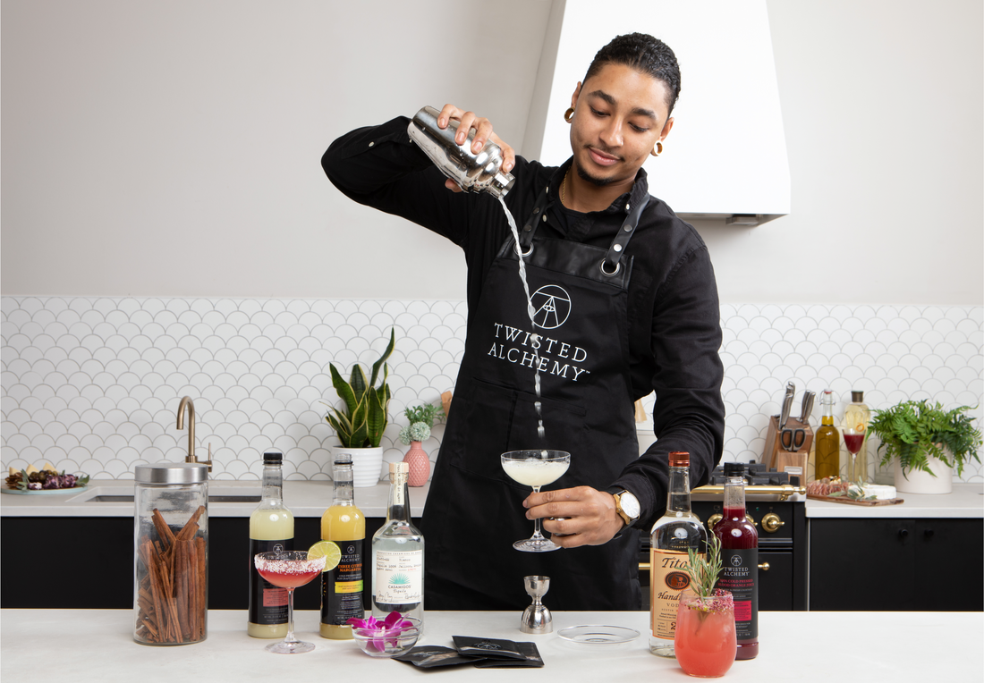 A bartender in a Twisted Alchemy apron pours a cocktail from a cocktail shaker