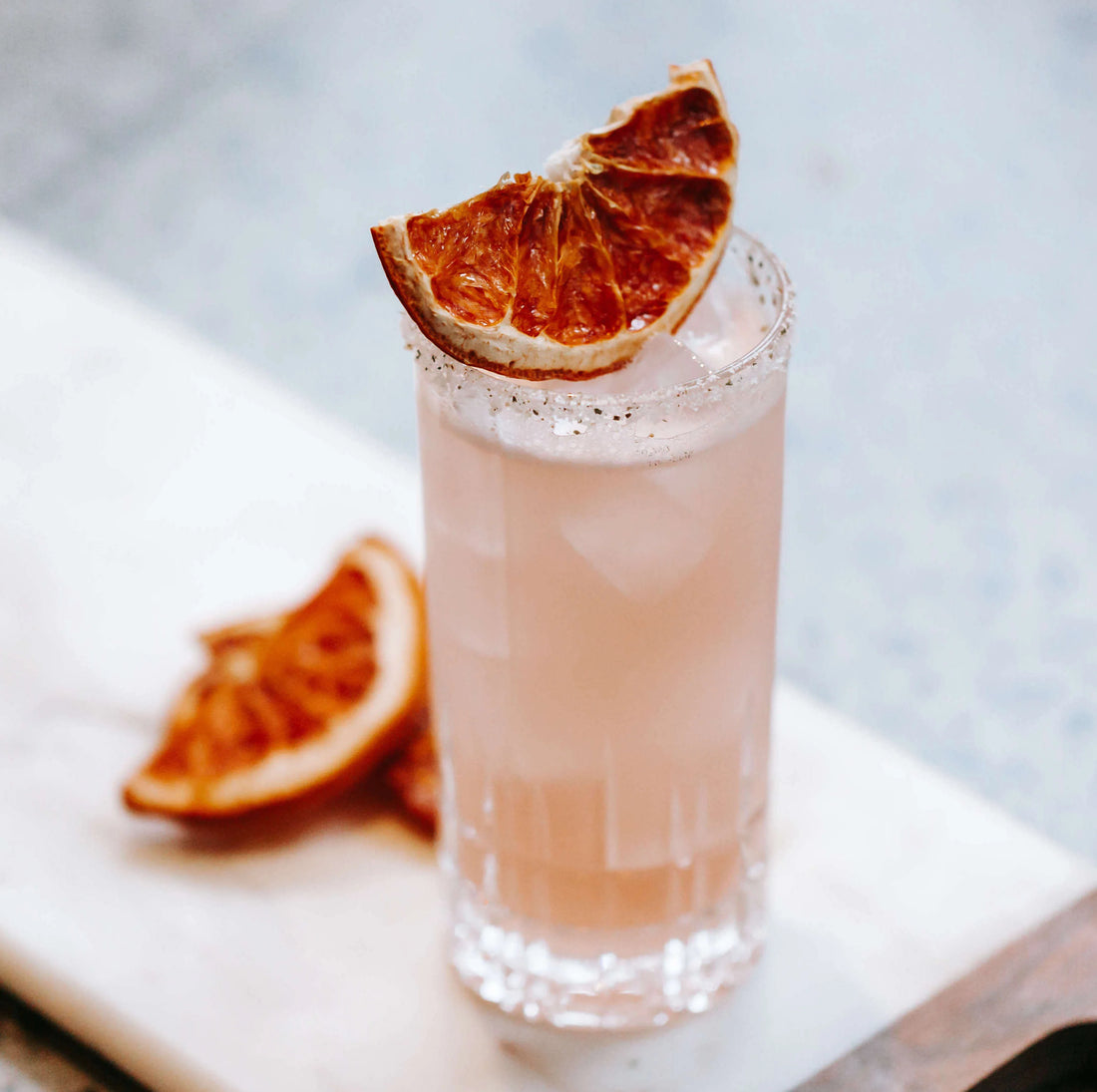 paloma shown in tall glass on white counter with dried grapefruit on top