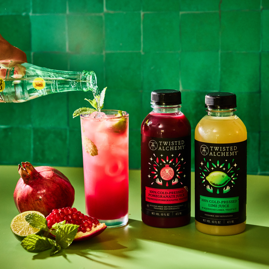 bright red pomegranate mojito with 2 twisted alchemy bottles next to it