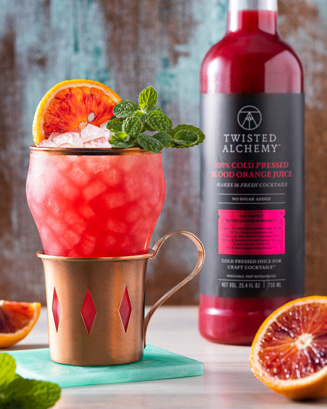 A cocktail in a copper mug next to a bottle of Twisted Alchemy blood orange juice