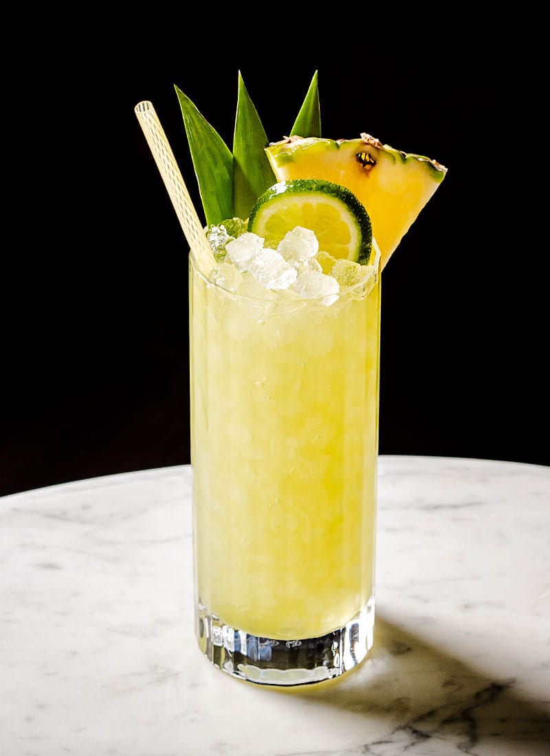 Pineapple cocktail sitting in a tall collins glass, resting on a slab of marble with a black background