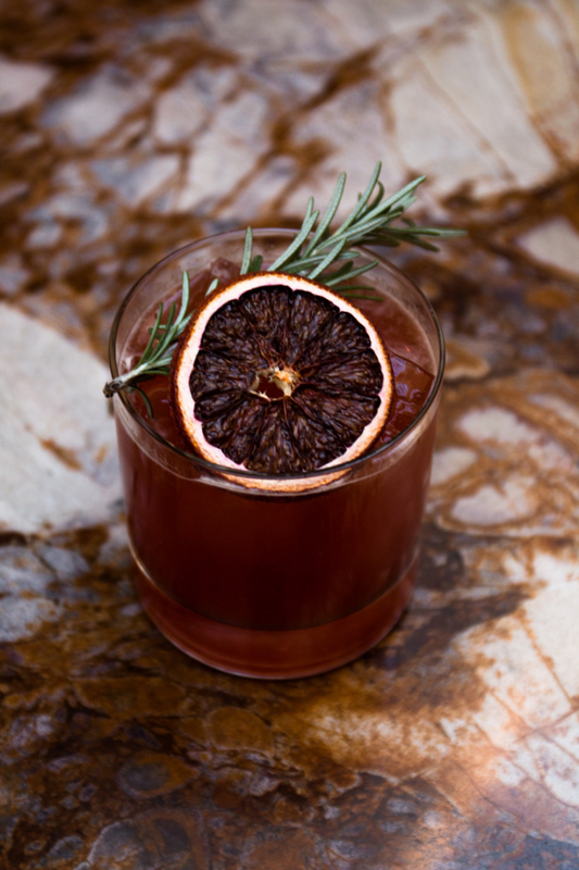 Blood orange cocktail with dried citrus wheel and fresh rosemary on top