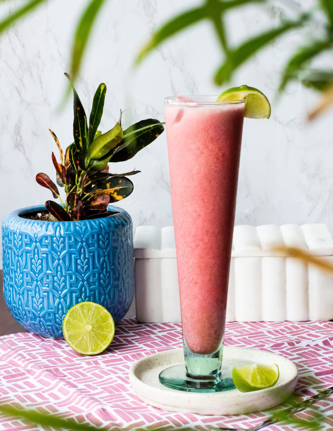 A pink smoothie with a lime wedge in front of a potted plant.