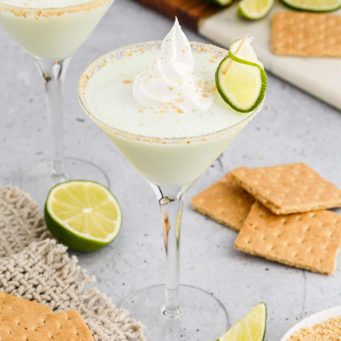 Key lime pie martini shown next to graham crackers with a lime slice on top and whipped cream