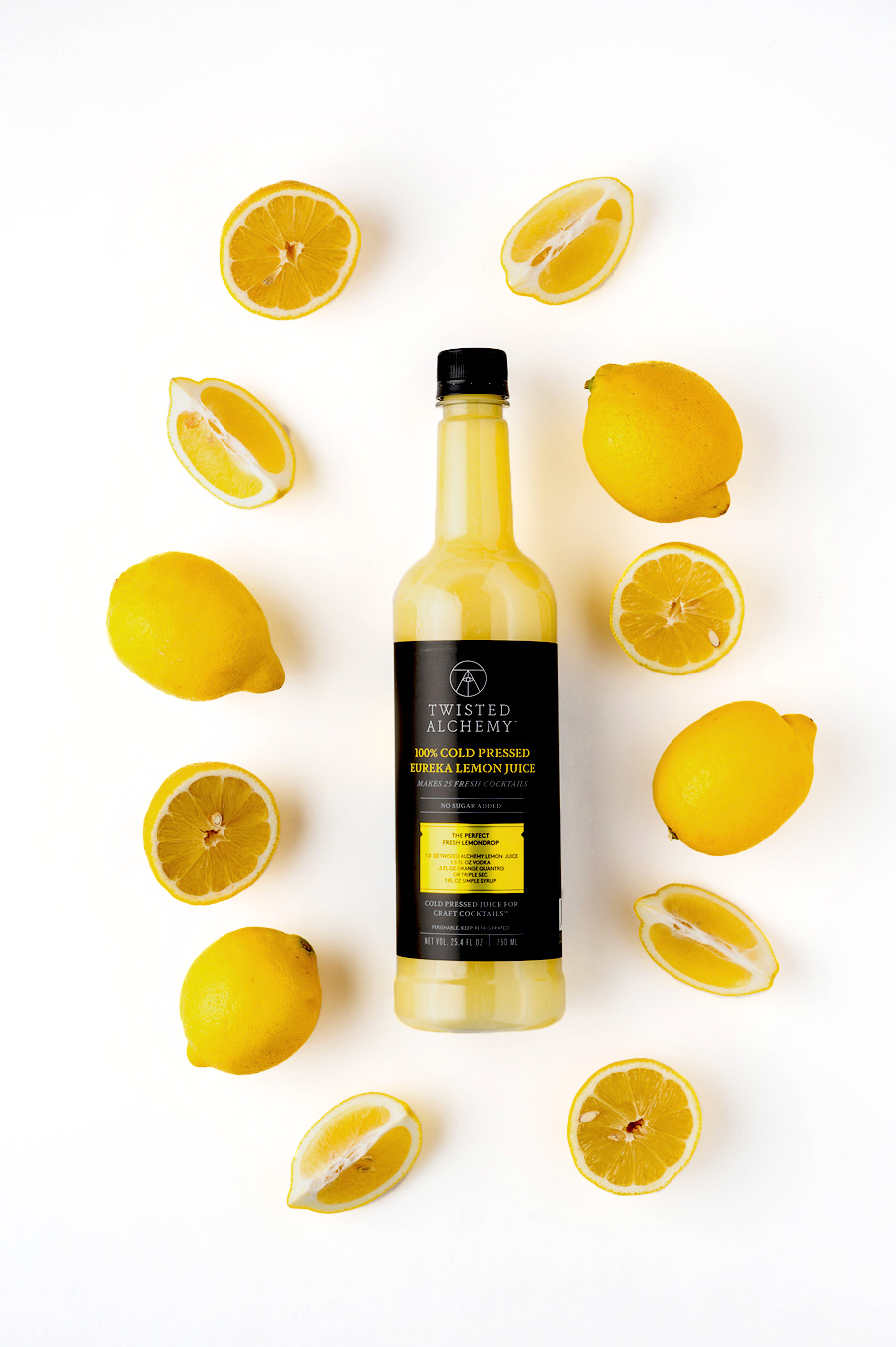 A bottle of lemon juice laid flat surrounded by various whole lemons, lemon halves, and lemon wedges against a white background.