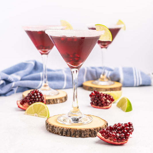 Pomegranate martini's featured on wooden circles with fresh pomegranate slices and lime slices featured around it