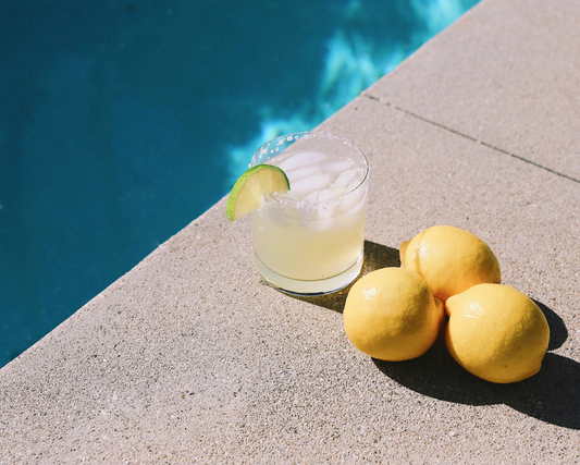 Lemonade Cocktail next to a pool with 3 lemons sitting to the right of it