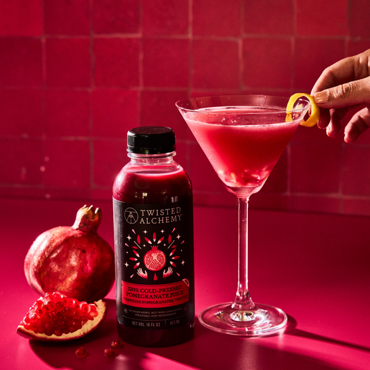Twisted Alchemy Pomegranate juice next to a red pomegranate martini styled with lemon garnish