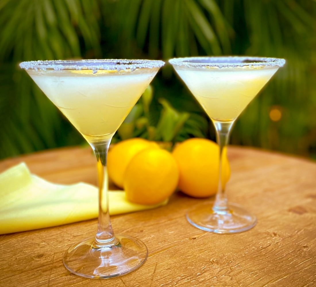 two lemon drop cocktails shown on wooden circular table with lemons in the background