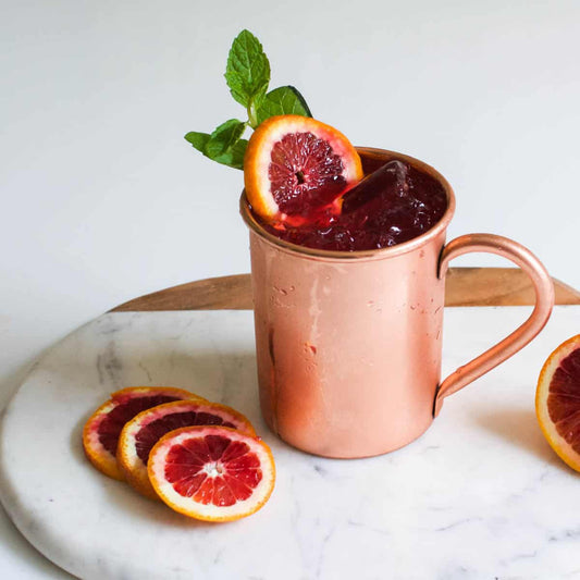 Blood orange moscow mule pictured on marble cutting board and mint in the glass against a white background