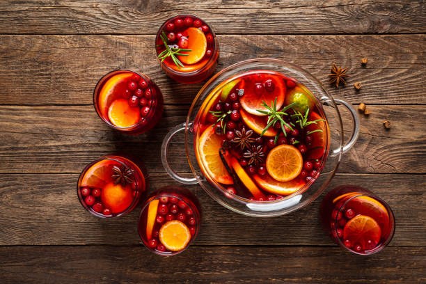 Punch bowl full of fruit, spices, and punch liquid surrounded by glasses full of punch and cranberries.