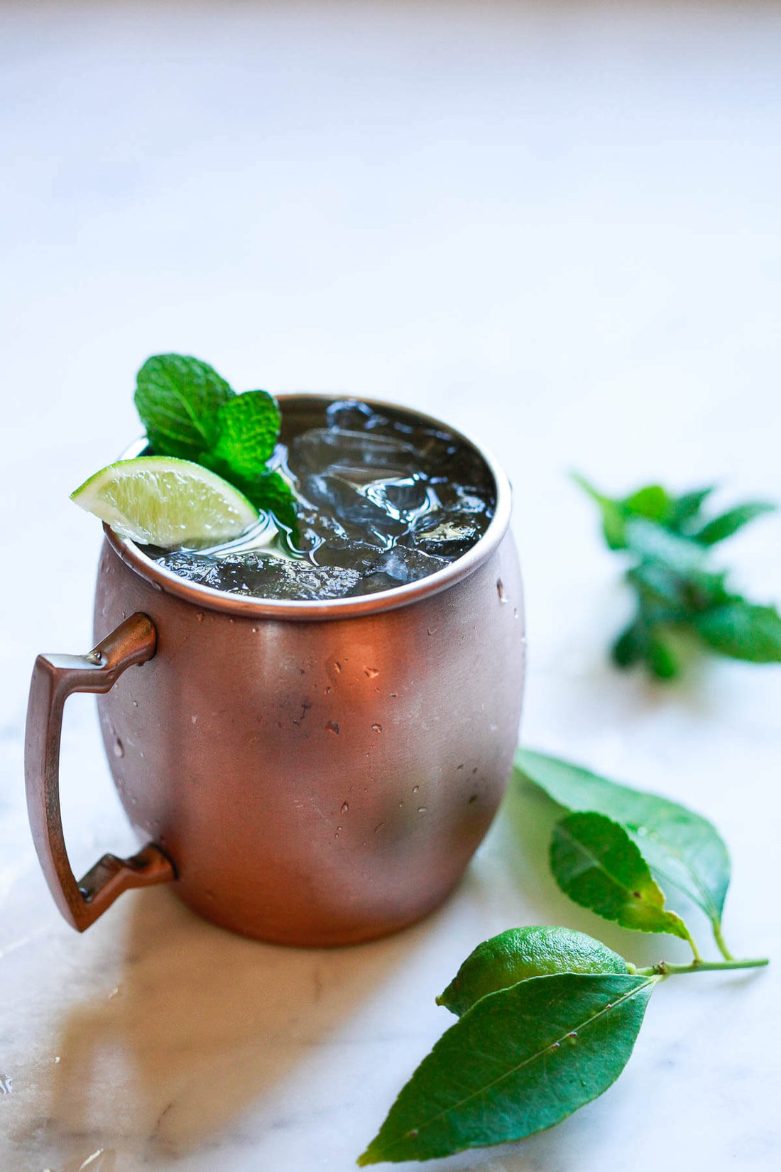 Moscow mule featured on white background with fresh mint laid around it