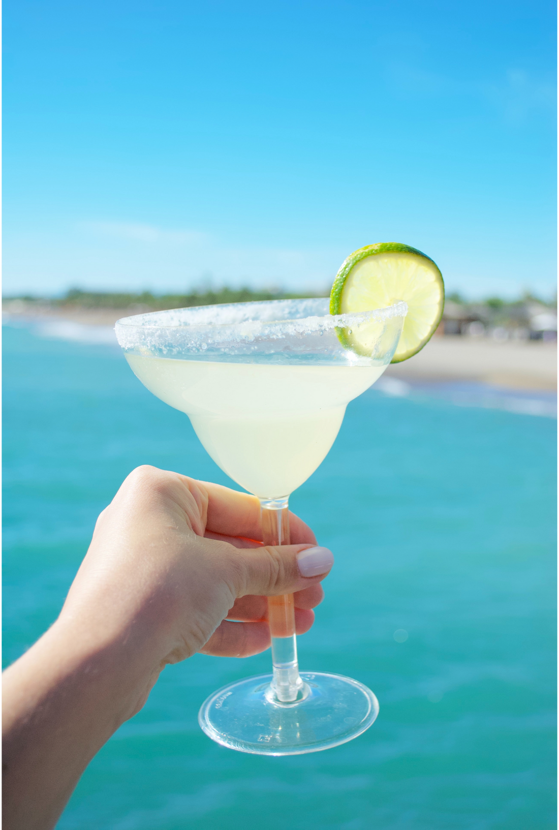 lime margarita in a hand against the background of a beach