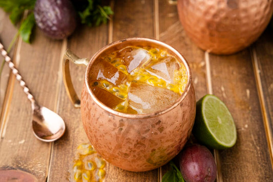 Passion fruit mule pictured on wood table with copper spoon to the left of it and a sliced lime to the right of it