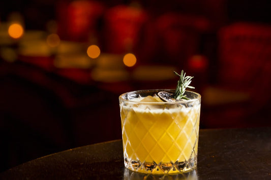 passionate cocktail shown with rosemary garnish on a dark background