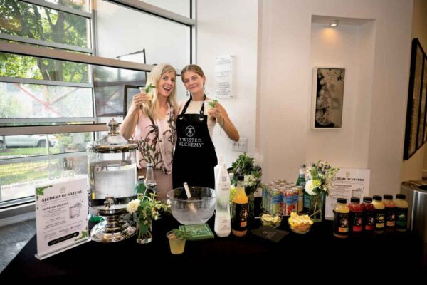 Two women behind a Twisted Alchemy table with various drinks and decor.