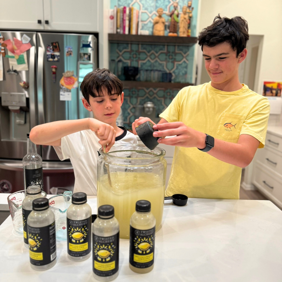 Two boys in a kitchen preparing a drink with Twisted Alchemy bottles on the counter.