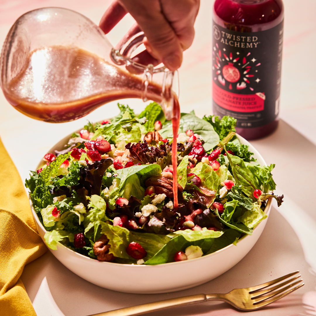 salad dressing being poured over a salad with a Twisted Alchemy juice bottle in the background