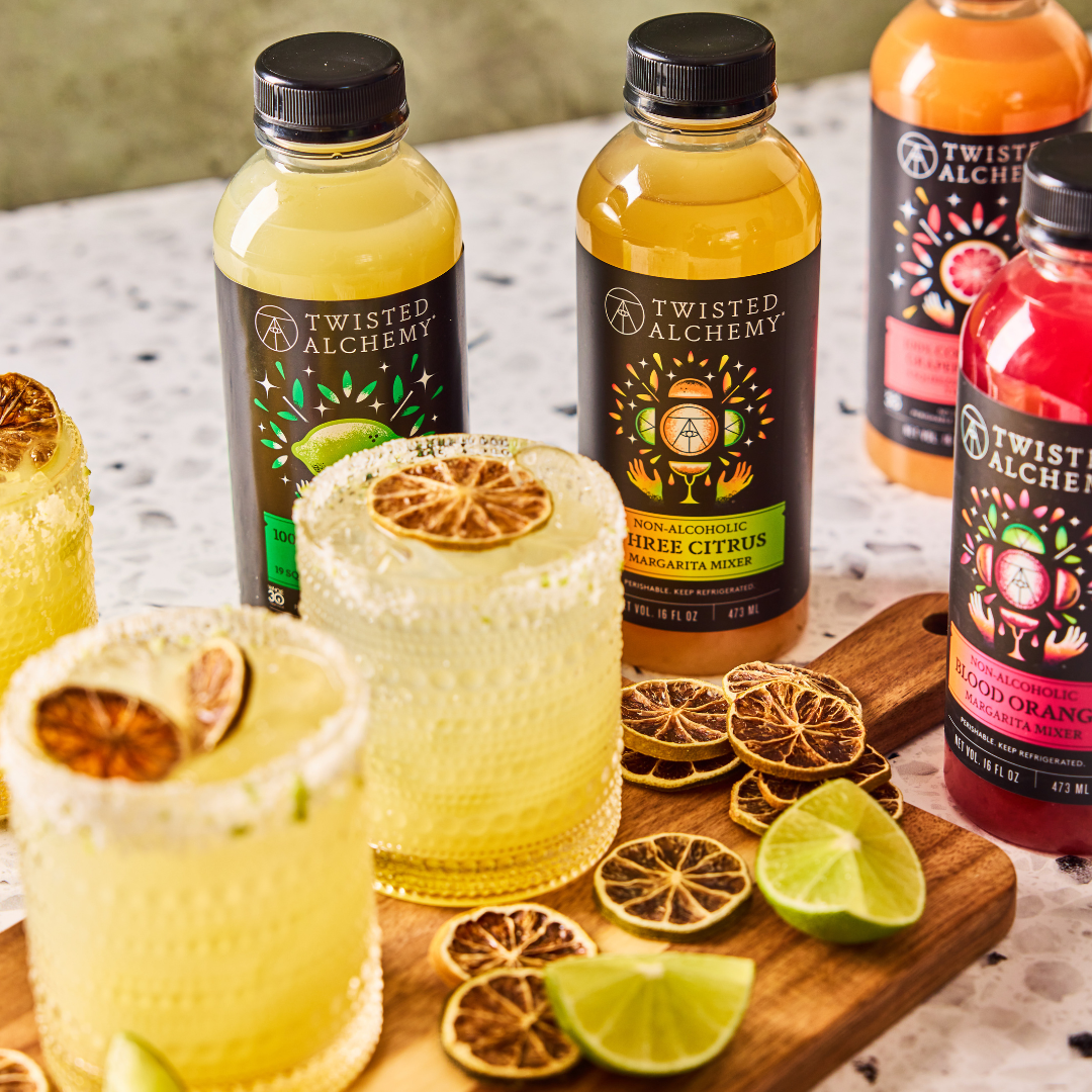twisted alchemy bottles sitting on a table with bright citrus cocktails