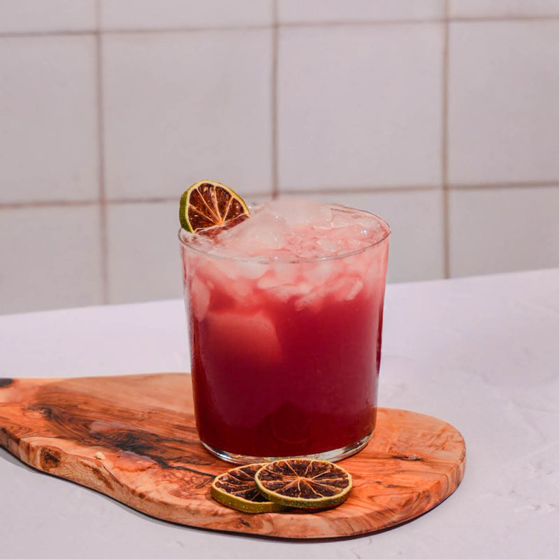 Red cocktail with lime garnish on a wooden board against a tiled wall background