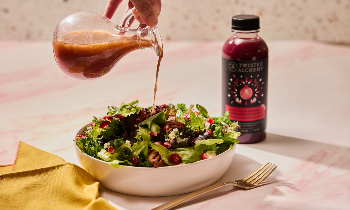 Person pouring salad dressing over a salad with Twisted Alchemy juice bottle in the background.