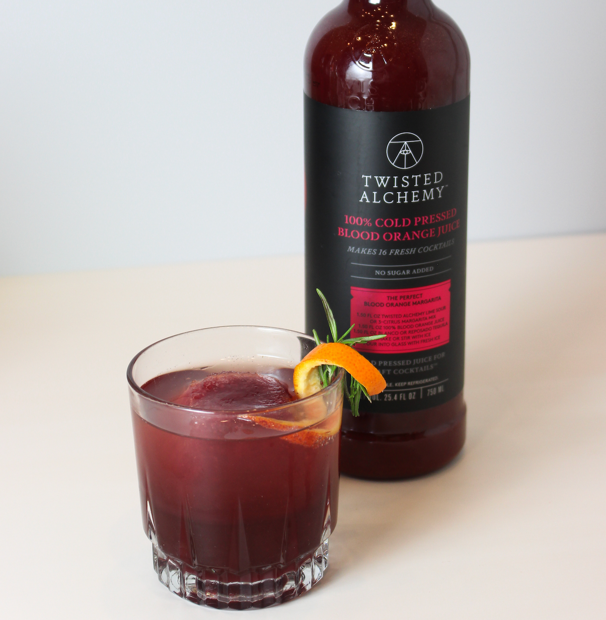 Bottle of twisted alchemy blood orange juice next to a blood orange cocktail