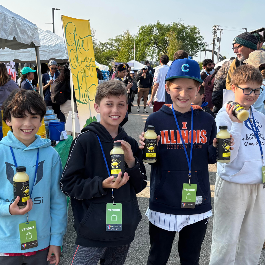 Children holding Twisted Alchemy bottles at an outdoor event with a crowd in the background