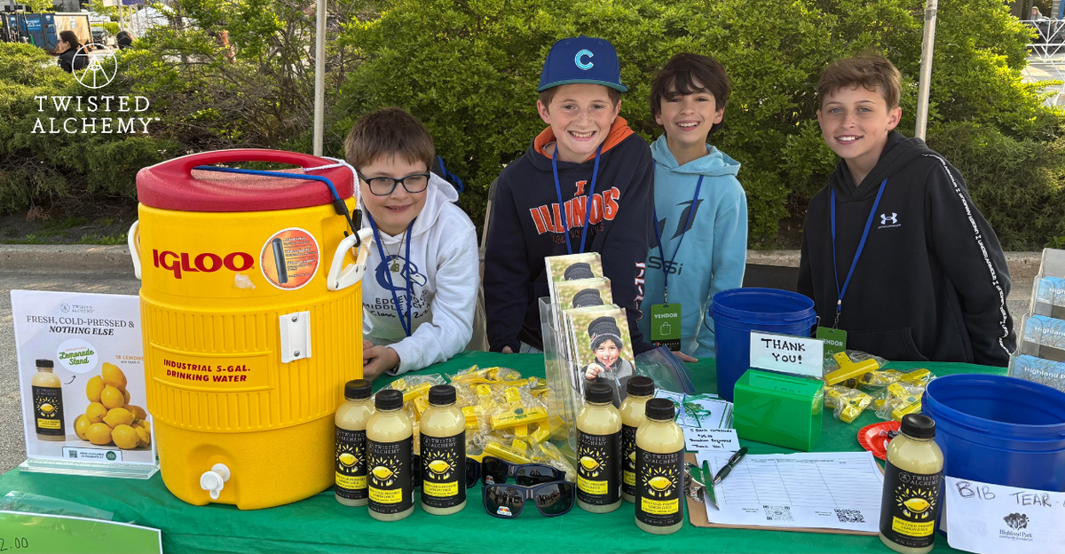 Four children standing behind a table with a yellow cooler and Twisted Alchemy bottles
