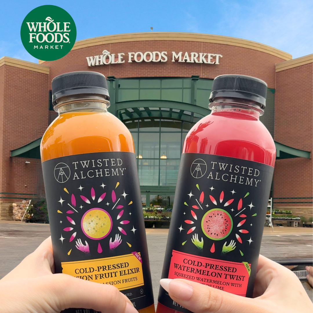 Two bottles of Twisted Alchemy juice held in front of a Whole Foods Market building.